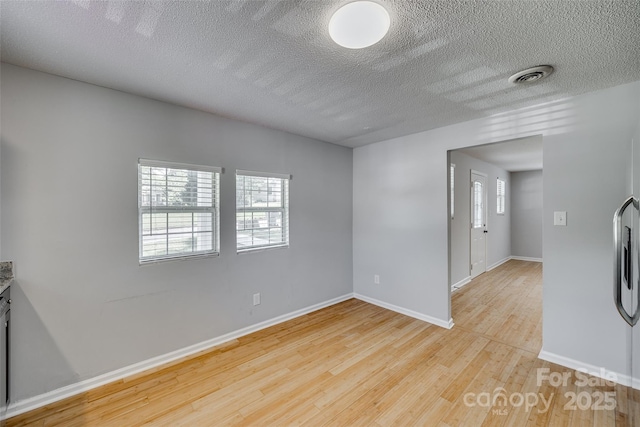 spare room with visible vents, a textured ceiling, baseboards, and wood finished floors