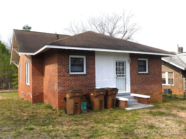 rear view of property with brick siding, entry steps, and a yard