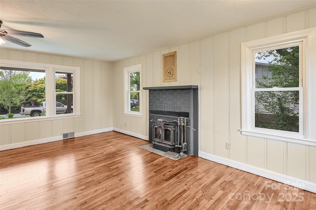 110 Maplewood Knoll Dr, East Flat Rock, NC 28726 - unfurnished living room with a wood stove, visible vents, light wood finished floors, a decorative wall, and a ceiling fan