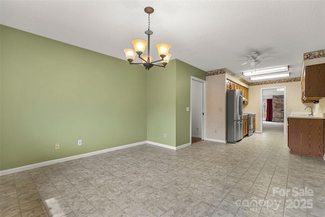 unfurnished room featuring ceiling fan with notable chandelier, a sink, a textured ceiling, baseboards, and light floors