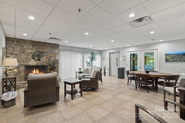 living area with a stone fireplace, french doors, visible vents, and a drop ceiling