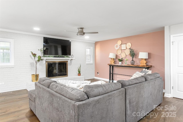 living room featuring ceiling fan, a brick fireplace, wood finished floors, and brick wall