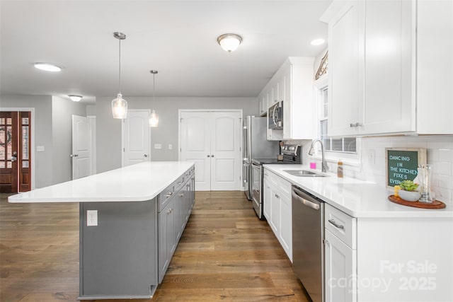 kitchen with a kitchen island, wood finished floors, white cabinets, stainless steel appliances, and a sink