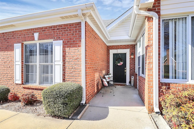 entrance to property with brick siding and a shingled roof