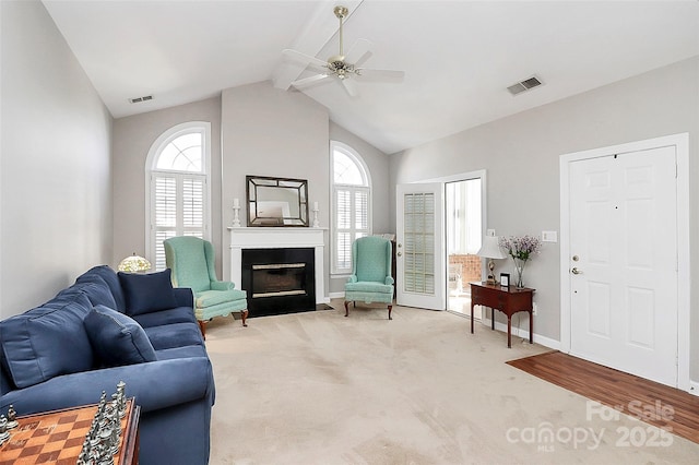 carpeted living area featuring a fireplace with flush hearth, a ceiling fan, visible vents, and vaulted ceiling with beams