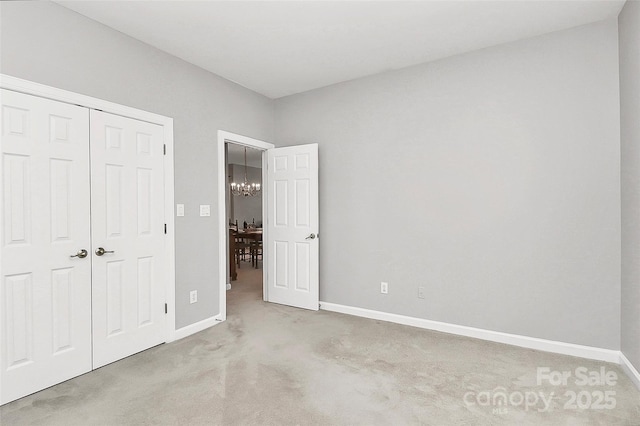 unfurnished bedroom with a closet, baseboards, a chandelier, and carpet flooring