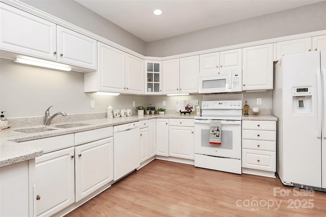 kitchen with white appliances, a sink, glass insert cabinets, white cabinetry, and light wood-type flooring