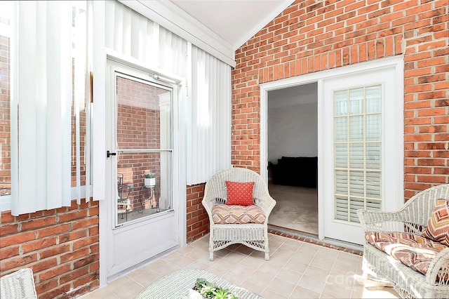 sitting room featuring lofted ceiling and brick wall