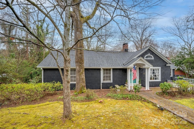 view of front of house featuring a chimney, a front lawn, and roof with shingles