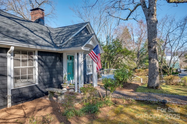 exterior space with fence, roof with shingles, and a chimney