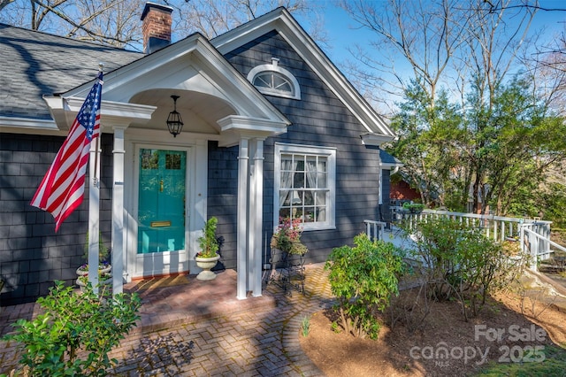 entrance to property featuring a chimney and a shingled roof