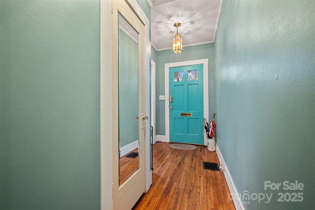 doorway with visible vents, ornamental molding, wood finished floors, baseboards, and a textured wall