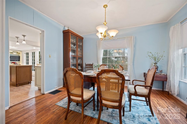 dining area featuring a chandelier, light wood finished floors, crown molding, and baseboards