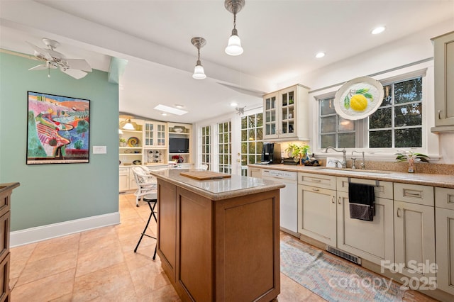 kitchen featuring a center island, glass insert cabinets, light countertops, white dishwasher, and a sink