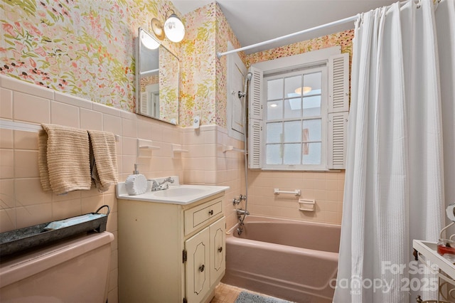 bathroom featuring wallpapered walls, shower / bath combo with shower curtain, wainscoting, tile walls, and toilet