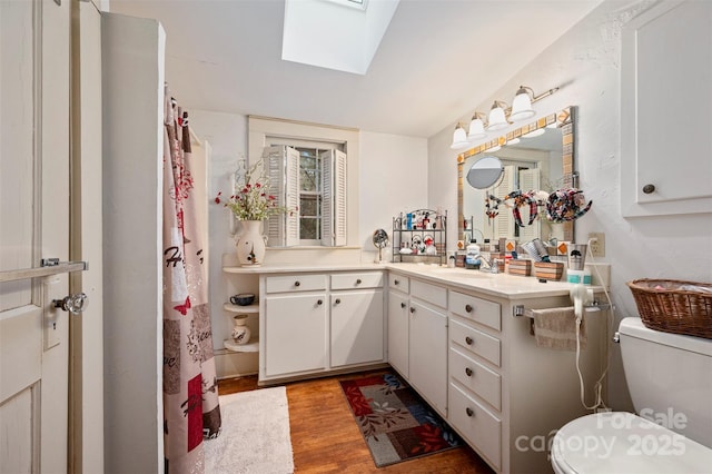 full bath featuring wood finished floors, toilet, a skylight, and vanity