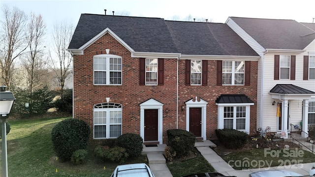 view of property featuring brick siding, a front yard, and a shingled roof