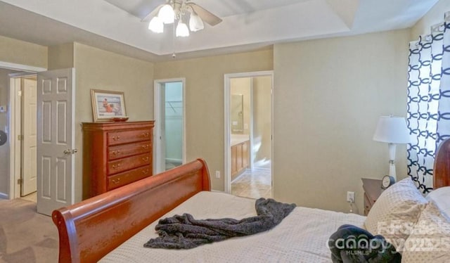 bedroom with ensuite bath, a tray ceiling, carpet flooring, and a ceiling fan