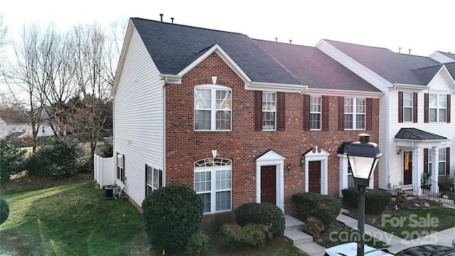 view of front of house with a front yard, brick siding, central AC, and a shingled roof