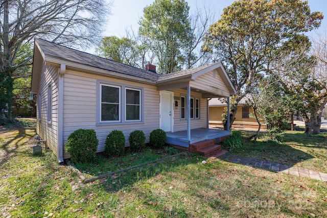 bungalow-style house with covered porch, a chimney, and a front lawn