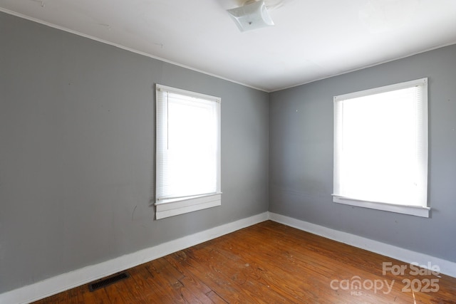 unfurnished room featuring visible vents, ornamental molding, baseboards, and wood finished floors