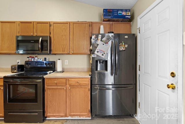 kitchen with light wood-type flooring, light countertops, appliances with stainless steel finishes, brown cabinetry, and a textured ceiling