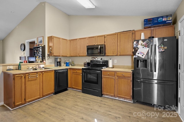 kitchen featuring light wood-type flooring, black appliances, a sink, a peninsula, and light countertops