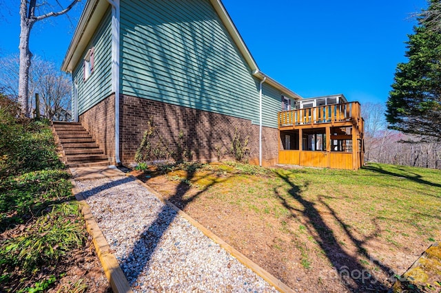 view of property exterior featuring a yard, brick siding, a wooden deck, and stairs