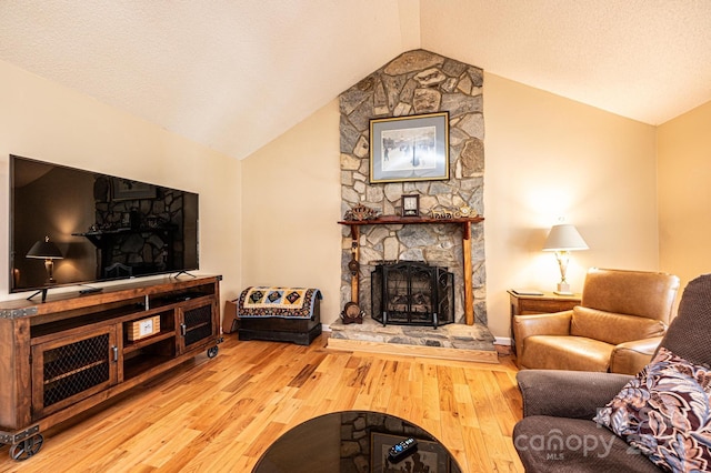 living room featuring a stone fireplace, vaulted ceiling, wood finished floors, and a textured ceiling