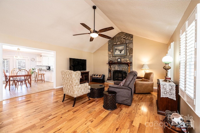 living area with vaulted ceiling, light wood-style flooring, a fireplace, a textured ceiling, and a ceiling fan