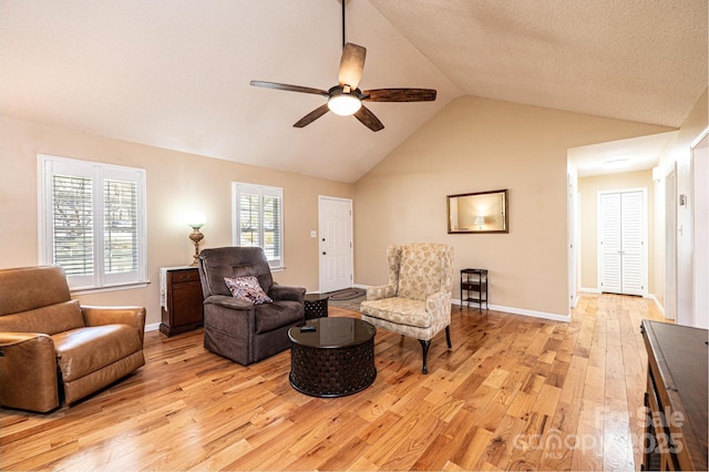 living area featuring baseboards, ceiling fan, light wood-type flooring, lofted ceiling, and a textured ceiling