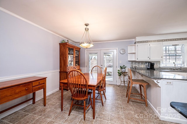 dining space with a wealth of natural light, french doors, ornamental molding, and wainscoting