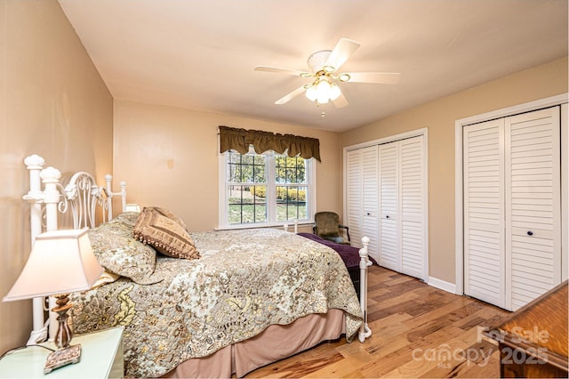 bedroom featuring a ceiling fan, wood finished floors, baseboards, and two closets