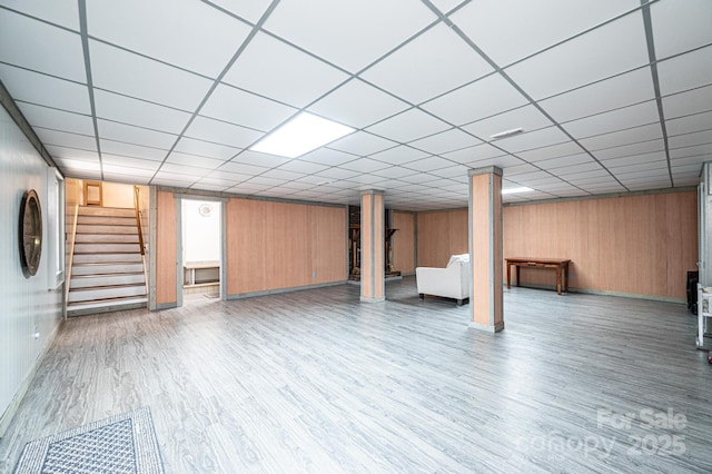 finished basement with stairway, a paneled ceiling, wooden walls, and wood finished floors