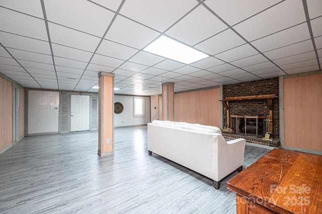 unfurnished living room featuring wooden walls, a brick fireplace, a paneled ceiling, and wood finished floors