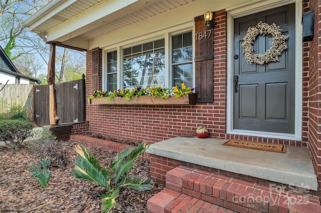 doorway to property with brick siding, a porch, and fence