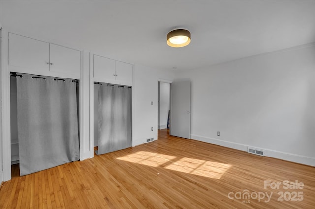 unfurnished bedroom featuring baseboards, light wood-style floors, visible vents, and multiple closets