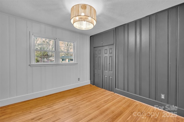 unfurnished bedroom with a closet, a textured ceiling, wood finished floors, and a decorative wall