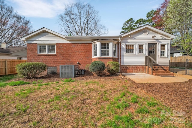 rear view of property with entry steps, central AC unit, brick siding, and fence