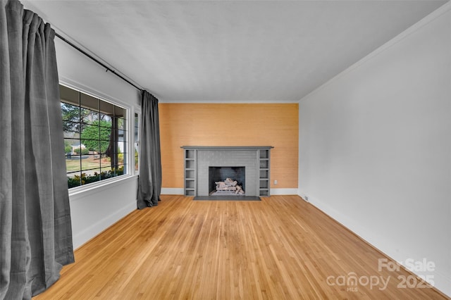 unfurnished living room featuring baseboards, a brick fireplace, wood finished floors, and ornamental molding