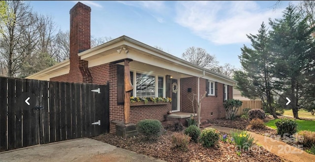 view of front of home featuring brick siding, a chimney, and fence