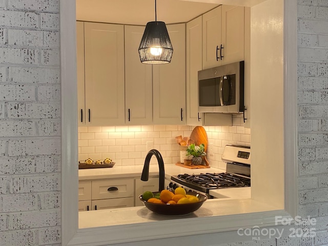 kitchen with pendant lighting, backsplash, white cabinetry, stainless steel appliances, and light countertops