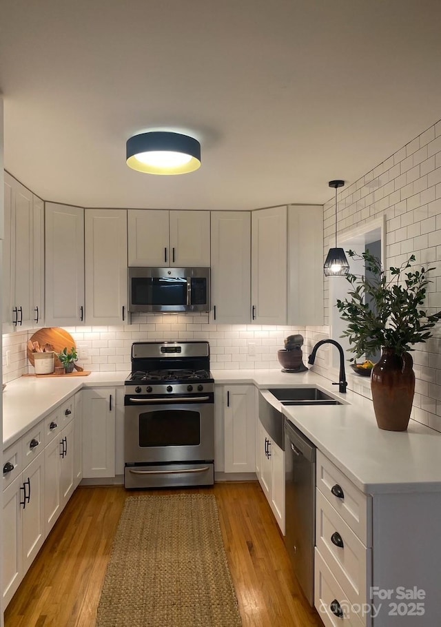 kitchen featuring a sink, stainless steel appliances, light wood-style floors, white cabinets, and decorative backsplash