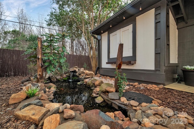 view of side of property with a small pond and fence