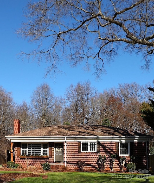 view of front of home with brick siding, a chimney, and a front lawn