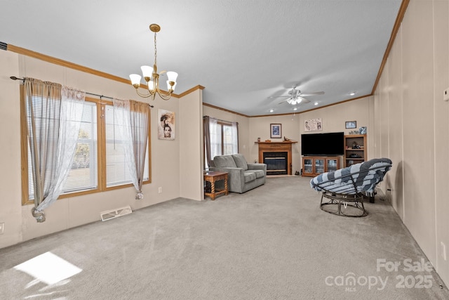 carpeted living area featuring visible vents, ceiling fan with notable chandelier, crown molding, and a glass covered fireplace