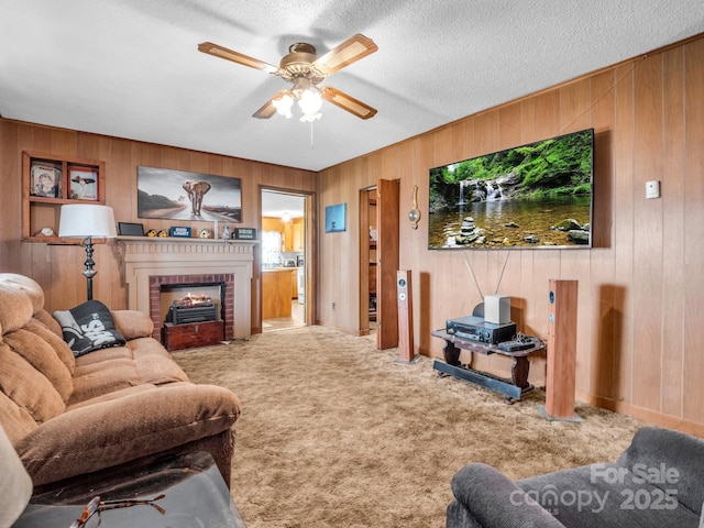 carpeted living area featuring a brick fireplace, wooden walls, a ceiling fan, and a textured ceiling