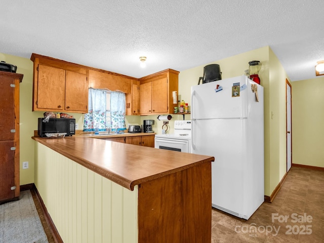 kitchen featuring black microwave, electric range oven, brown cabinets, a peninsula, and freestanding refrigerator