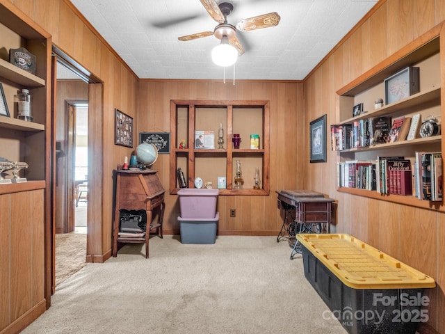 carpeted office with wooden walls, ceiling fan, a wood stove, and crown molding