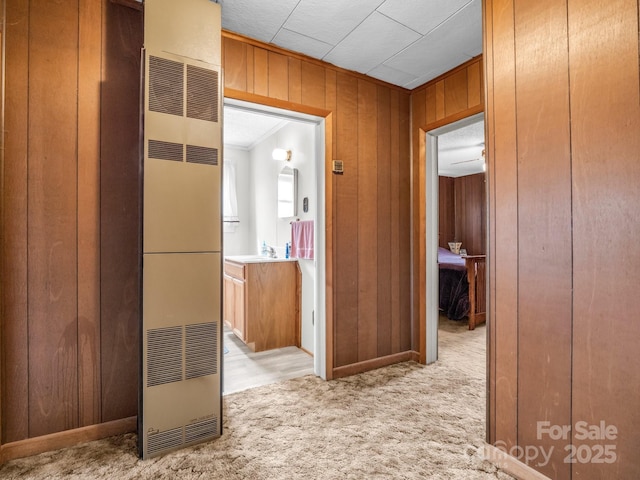 hall with a sink, wood walls, crown molding, carpet flooring, and a heating unit